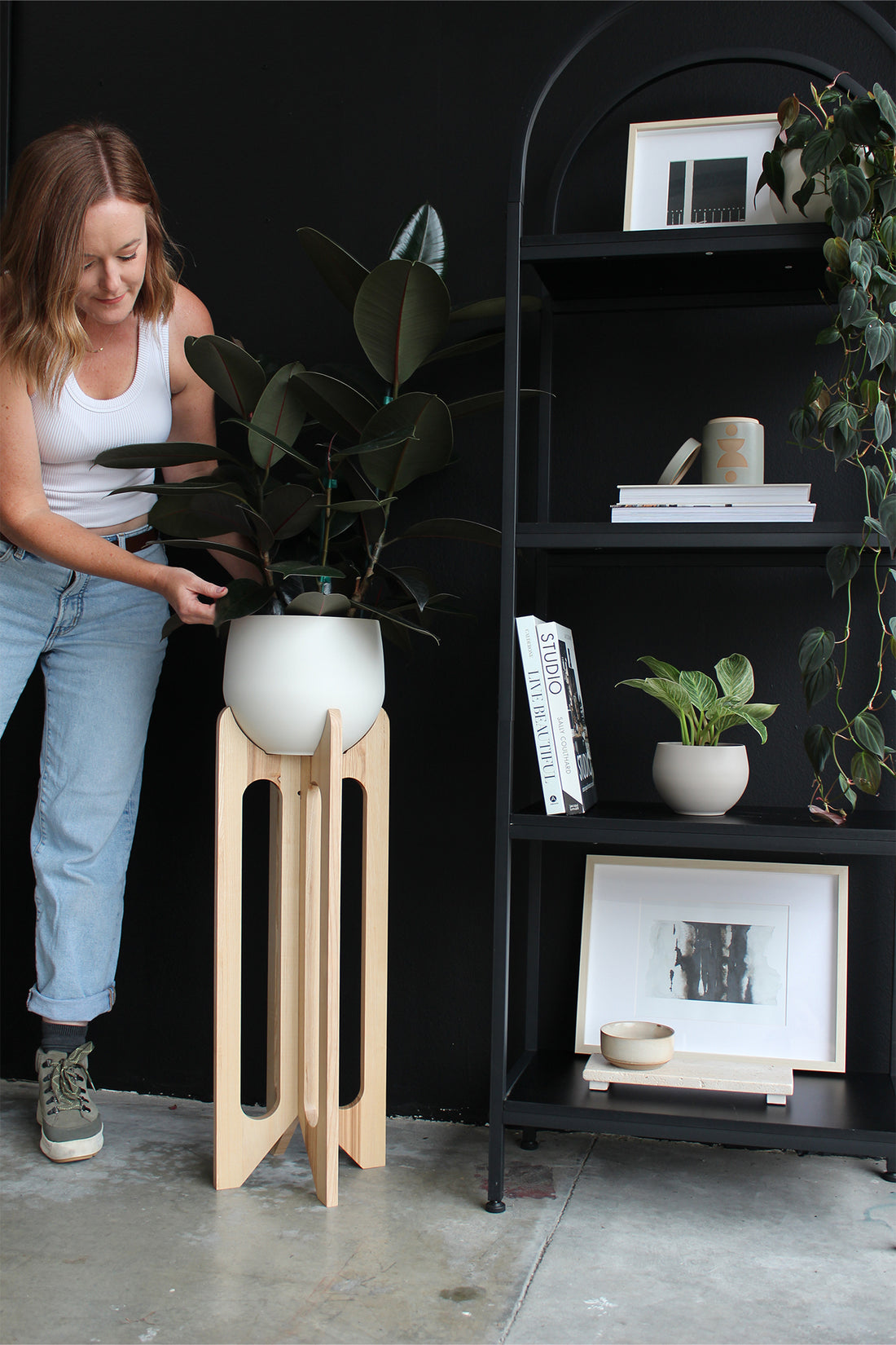 person placing pot on tall modern wood plant stand