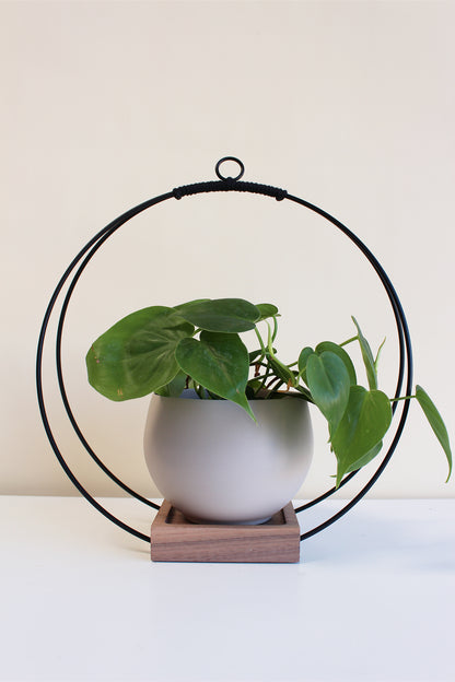 large circular hanging planter with matte black rings and walnut wood base and tan colored aluminum pot for houseplants